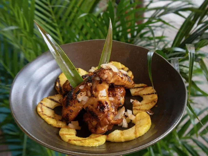 Hulihuli Chicken Wings at Voyagers in Kailua-Kona: fire-roasted wings over grilled pineapple rings with diced onion, in a stoneware bowl
