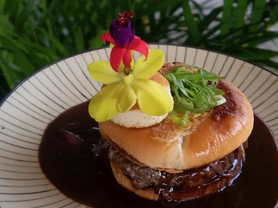 Loco Moco Burger at Voyagers in Kailua-Kona: a wagyu patty on a toasted bun in a pool of house gravy, topped with an over-easy egg, green onion and an orchid