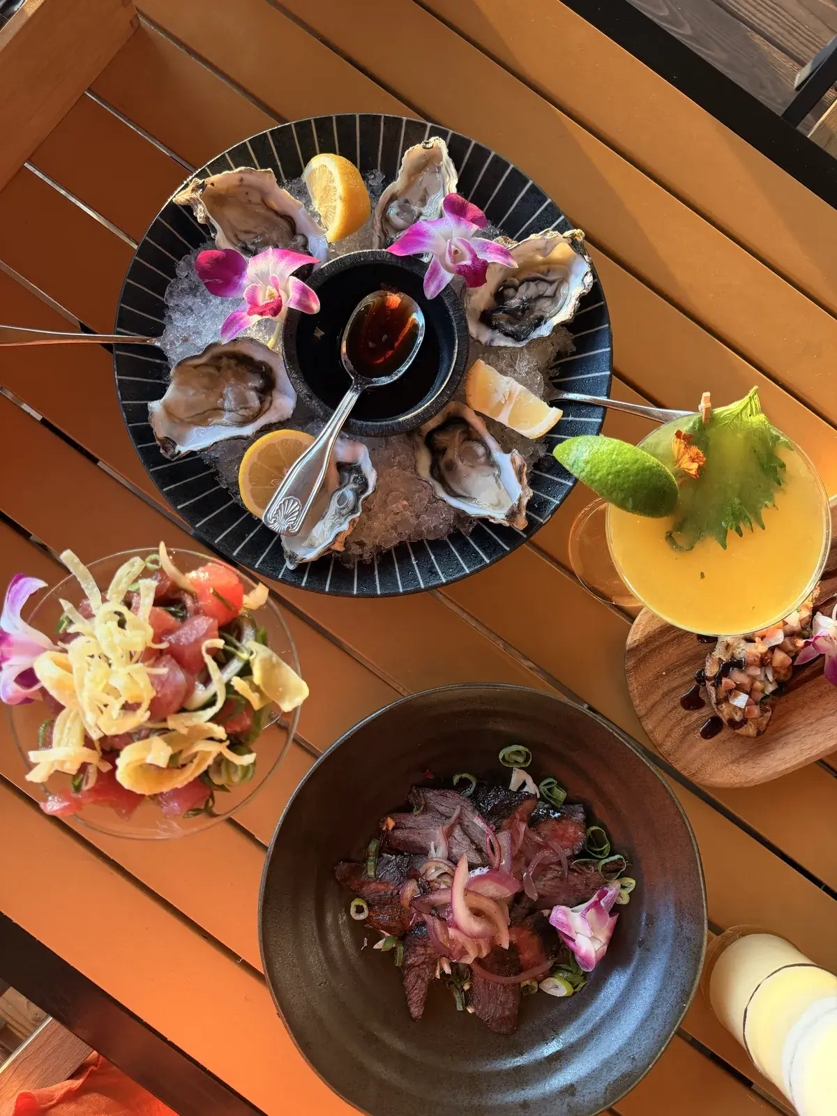 Pupus and cocktails from above at Voyagers in Kailua-Kona: fresh oysters on ice with orchids and chili-soy sauce, ahi poke parfait with crispy wonton strips, sliced steak with red onion and a cocktail with lime and shiso