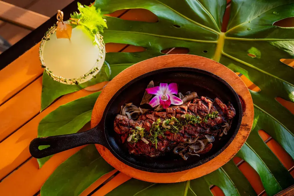 Sizzling New York Steak at Voyagers: a New York strip on a cast iron skillet with sautéed onions and chimichurri