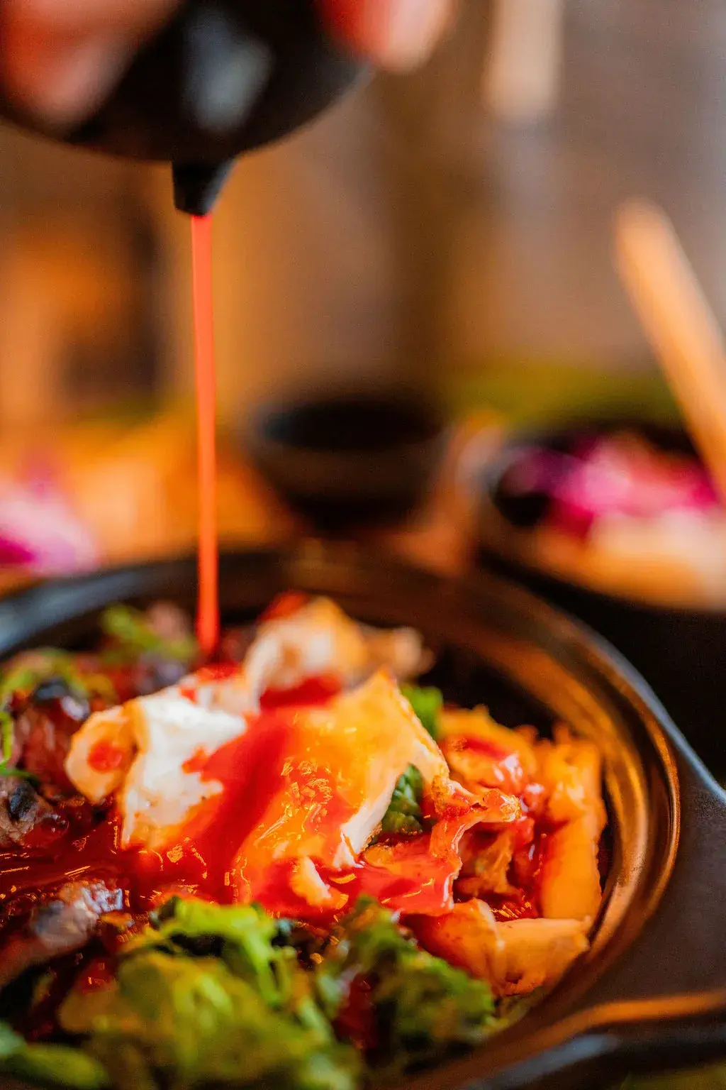 Gochujang sauce poured over the Voyagers Korean Bowl in its hot pot