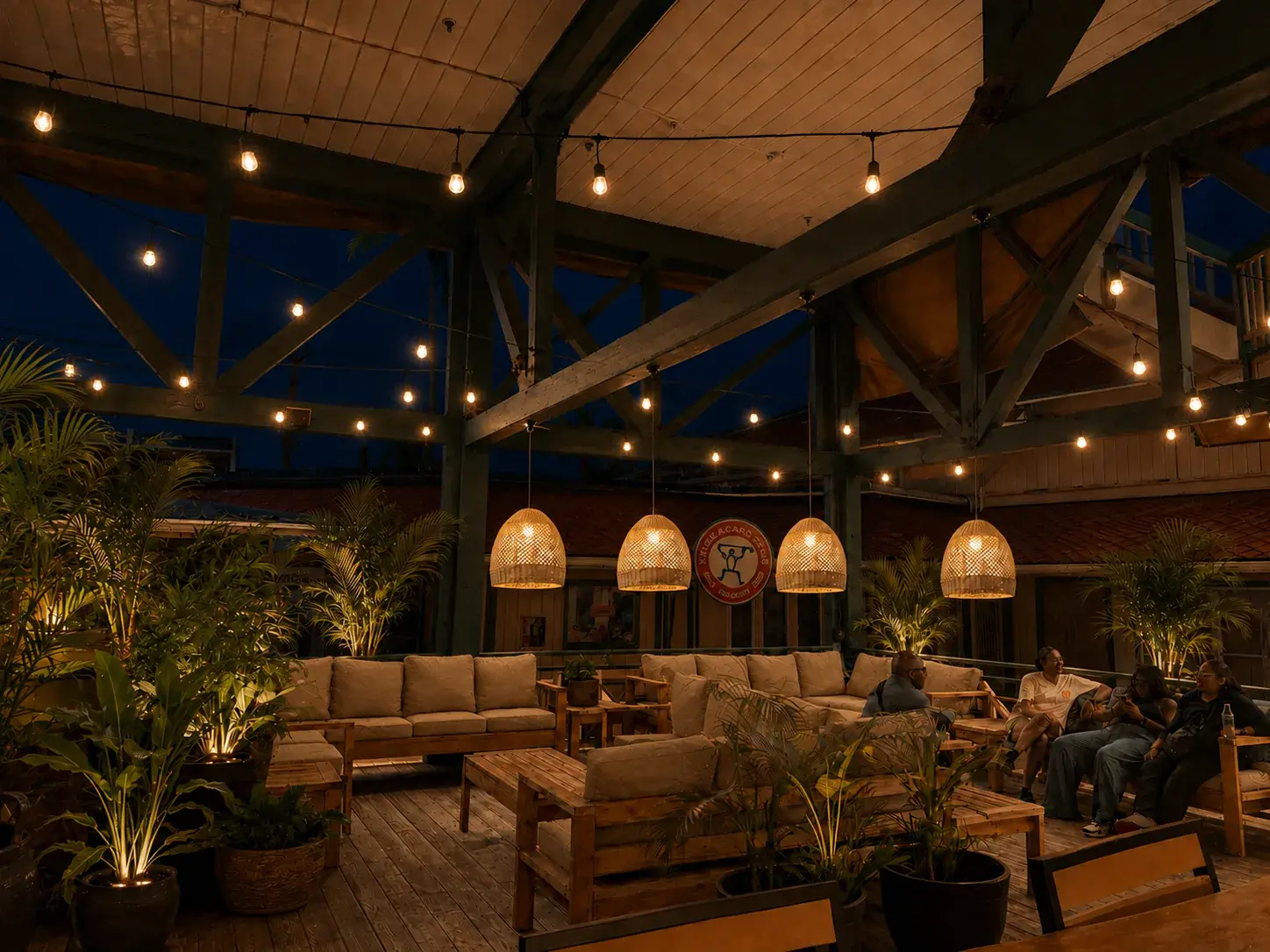 Open-air lanai lounge at Voyagers at dusk, with woven pendant lamps, string lights strung between timber trusses, teak sofas and potted palms